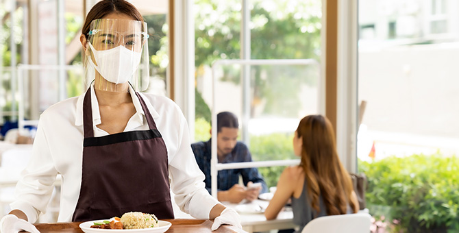 Food service worker wearing a mask and face shield while holding a tray of food