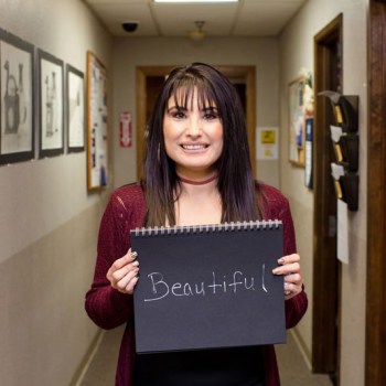 Woman smiling in a hallway with an oversized card reading: beautiful