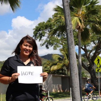 Woman outdoors smiling and holding an oversized card reading: hope