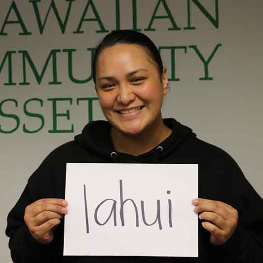 Woman smiling in a room holding an oversized card reading: lahui