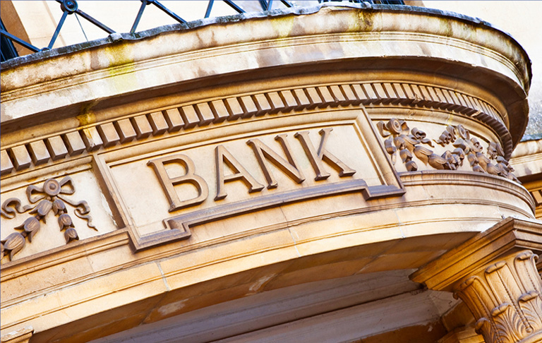 the top of the front entrance of a bank with gold detailing and the word bank in the center