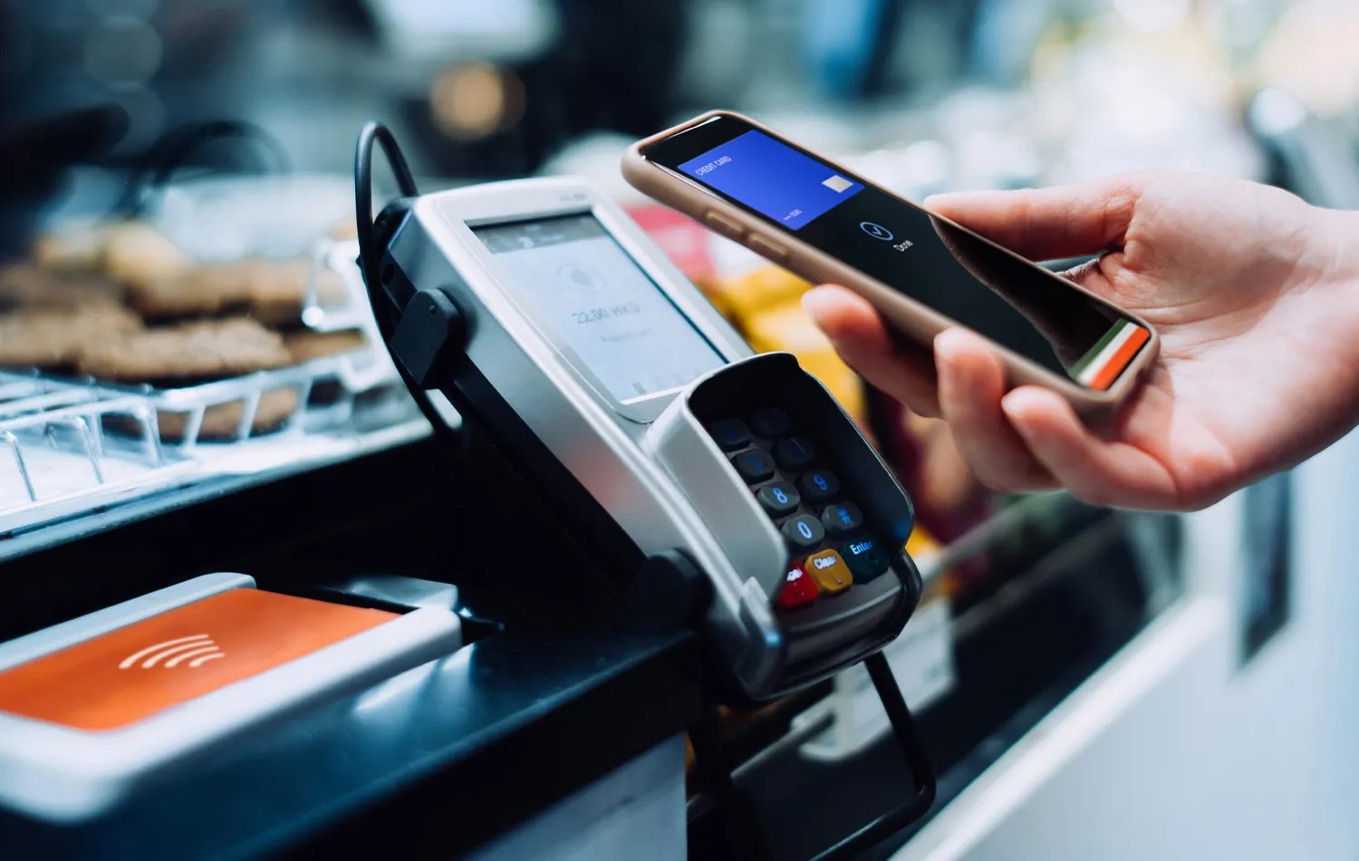 a person holding a smartphone in front of a card readers and using the tap to pay feature