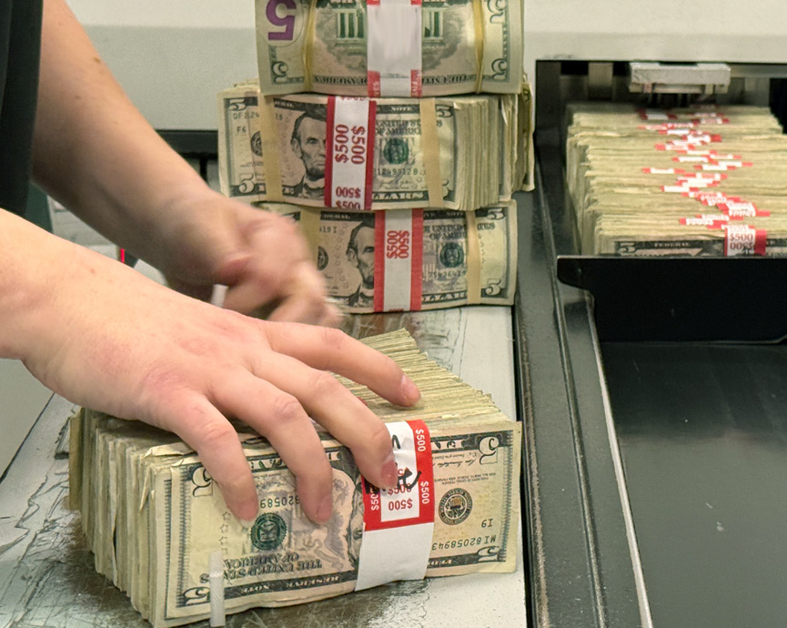 Person handling stacks of five dollar bills.