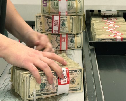 Person handling stacks of five dollar bills.