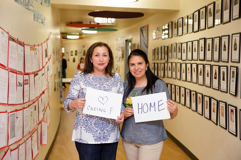 Connie Snowden and Adelita Jasso hold signs reading Caring and Home