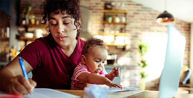 Mother having breakfast and doing bills with her baby in her lap