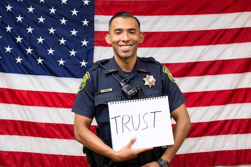 Firebaugh Police Officer Fernando Moreno holds sign reading Trust