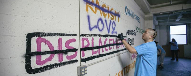 Man painting the word Love over the word Displacement, which is crossed out