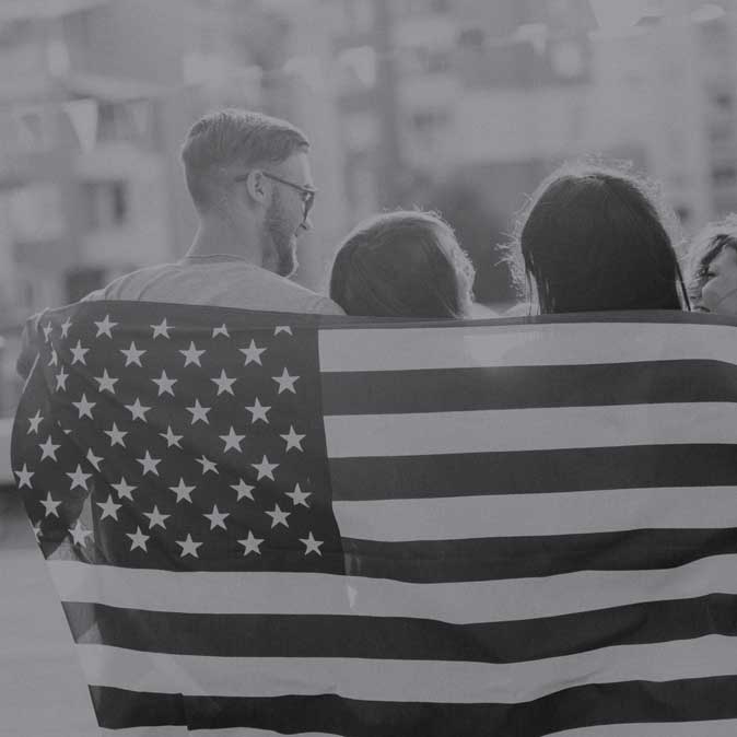 Image of a man and two females with backs turned and drapped with the American Flag