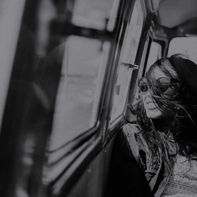 Young smiling female with sunglasses rests in a passenger seat looking out the window with the wind bursting through her hair