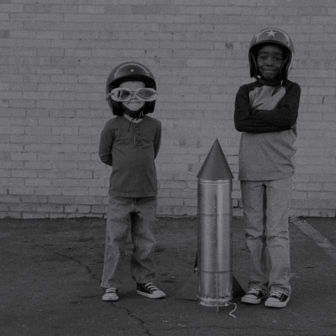 Two young boys standing with a toy rocket between them.