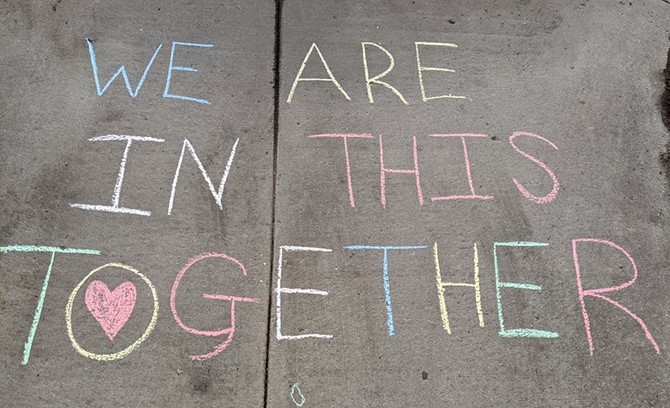 ‘We are in this together’ written in colored chalk on a sidewalk